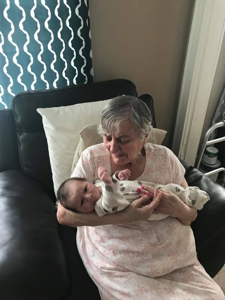 An elderly woman holding a newborn, symbolizing generations of caregiver care and connection