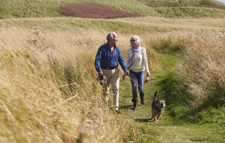 Caregiver and spouse walking their dog on a scenic trail