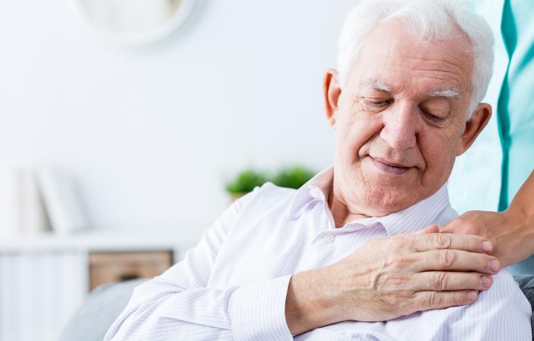 An elderly man touching his caregiver's hand on his shoulder