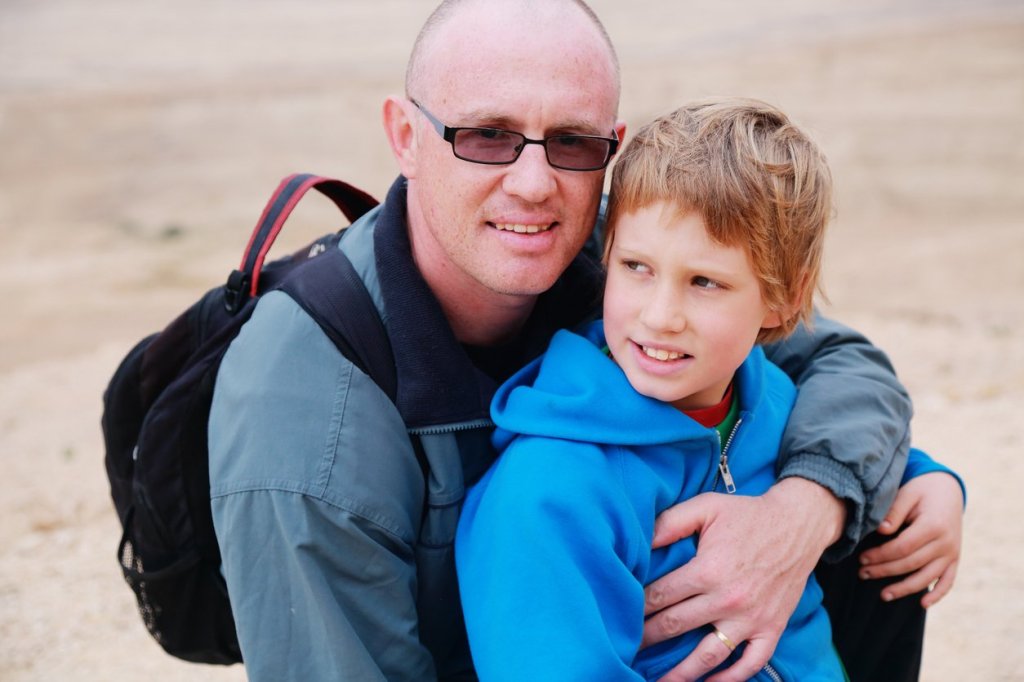 Loving father embraces his autistic son from behind, showcasing compassion and support in caregiving