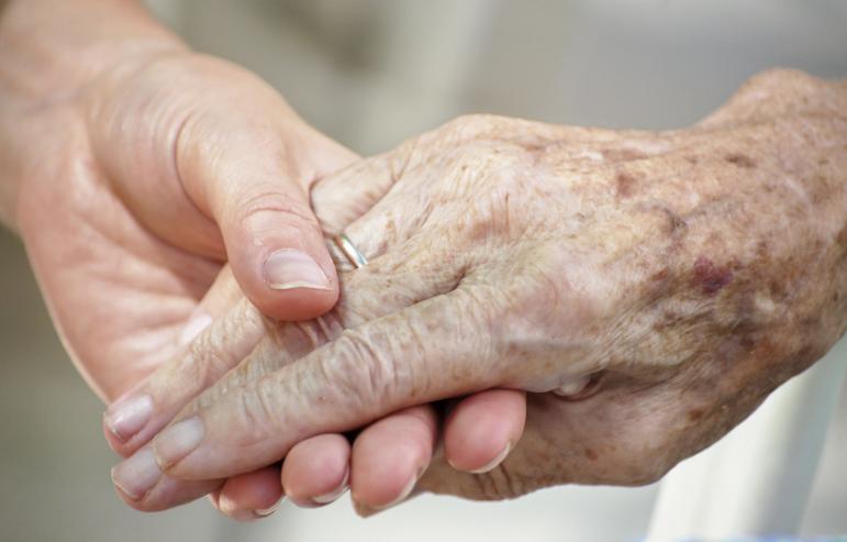 A caregiver holding their elderly loved one's hands