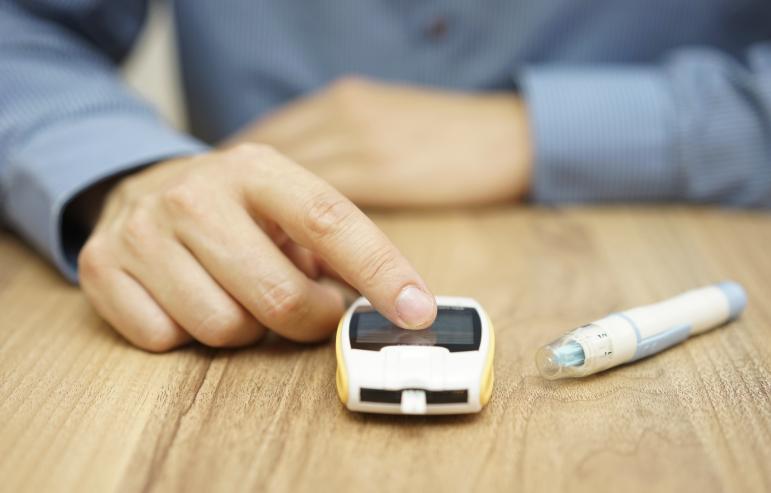 A caregiver waiting for the results of finger-stick blood test with an insulin pen laying nearby