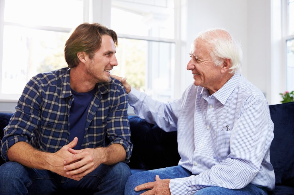 A caregiver son happily sitting with his elderly father