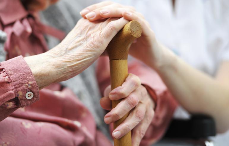 A caregiver and her loved one resting their hands on a cane