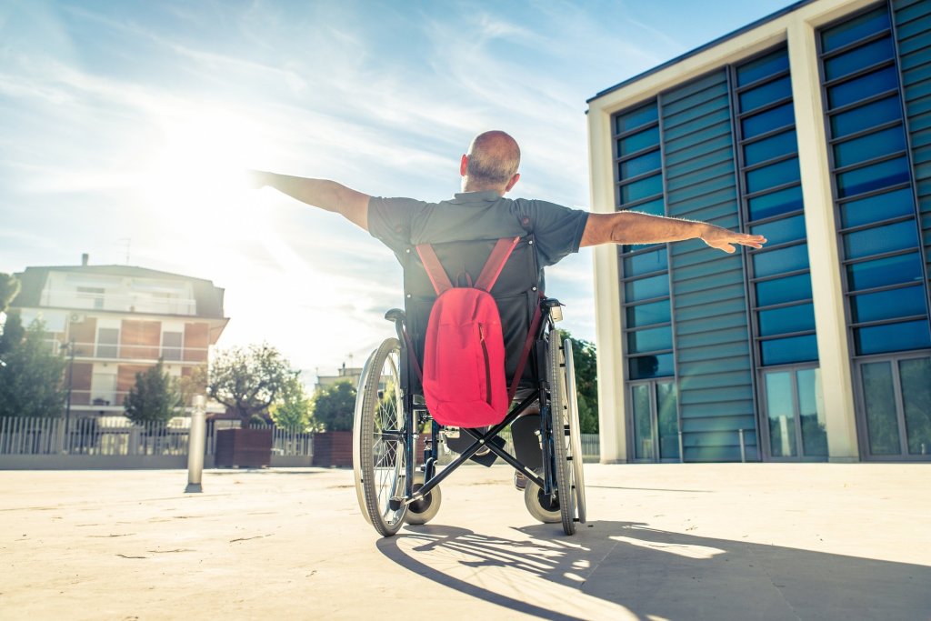 A wheelchair-bound man spreading his arms while gazing into a bright scenic area