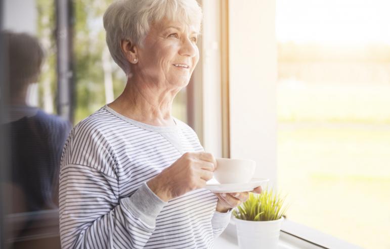 A caregiver holding her tea while she happily gazes out the window