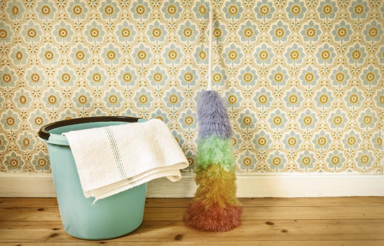 A bucket, duster, and towel on a wooden floor next to a wall