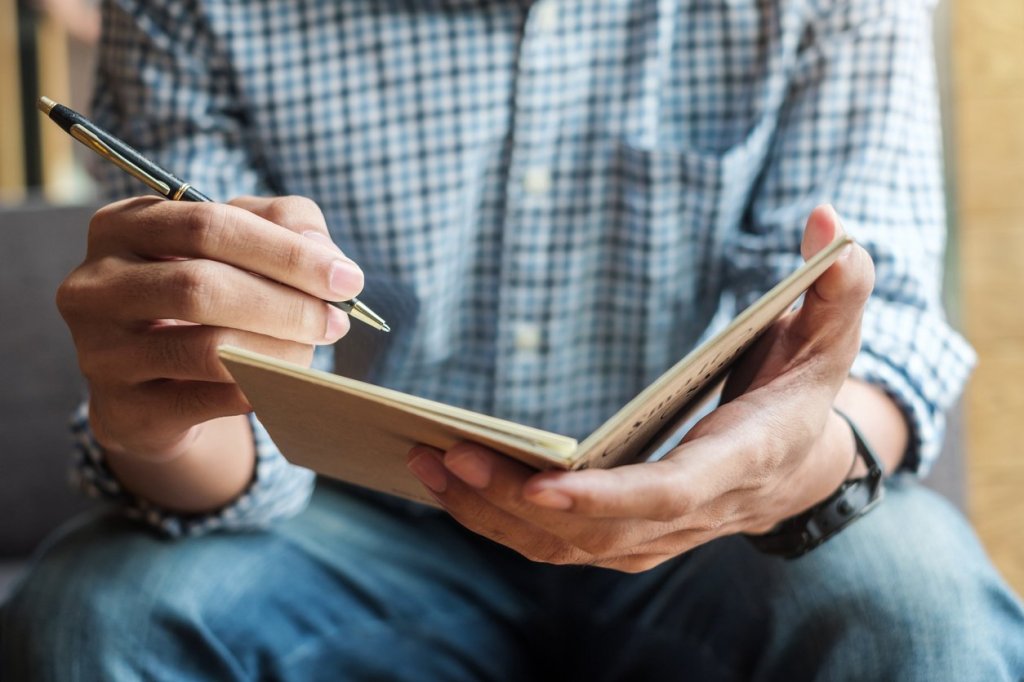 A man is writing in a notebook to aid in the recovery process from traumatic brain injury