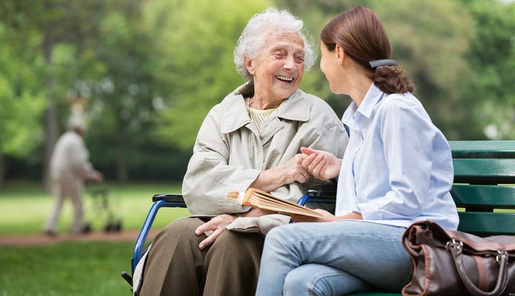 Elderly lady seated with a caregiver on a park bench