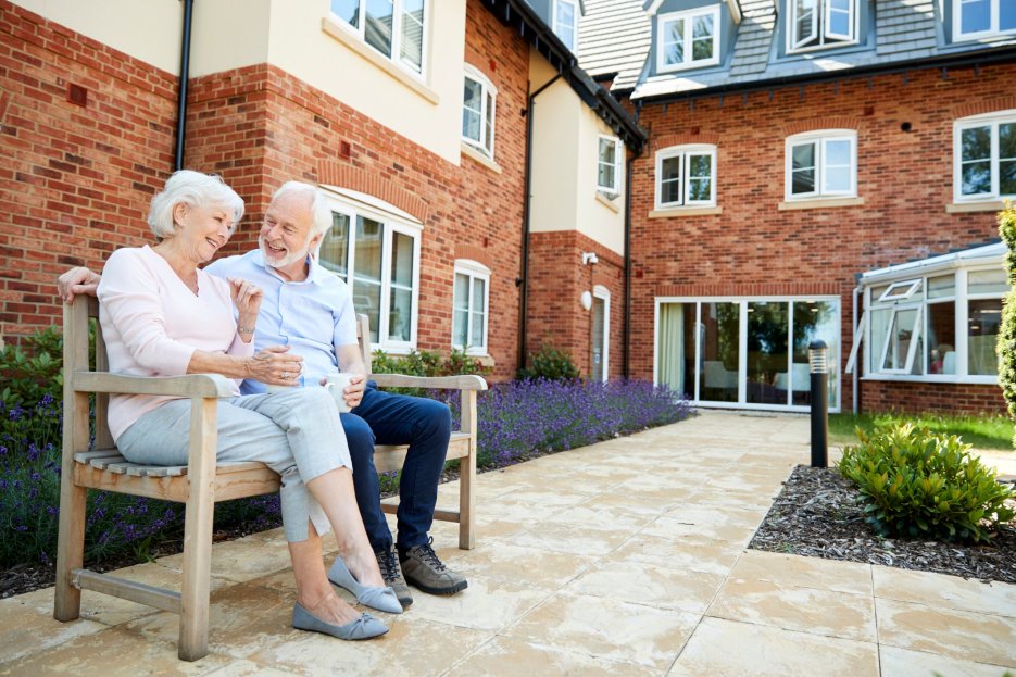 A caregiver and his wife happily sitting on a bench outside