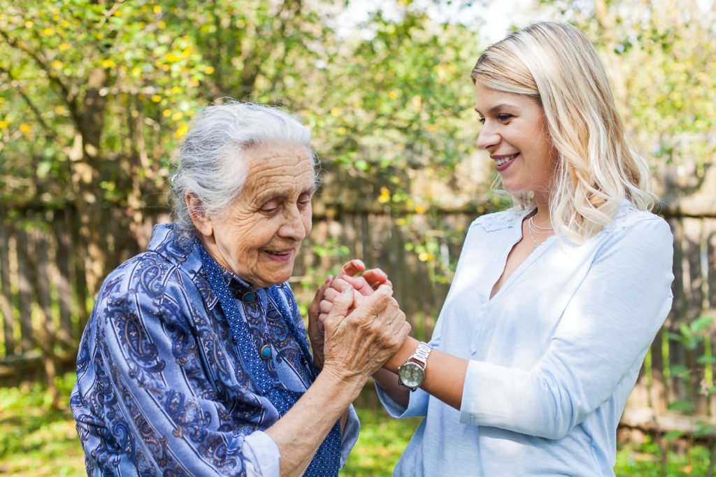 Smiling caregiver daughter holding hands with her aging mother