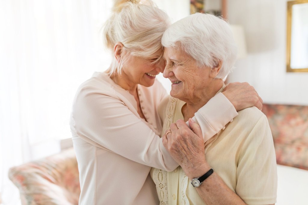 A caregiver daughter smiling with her elderly mother as they hug