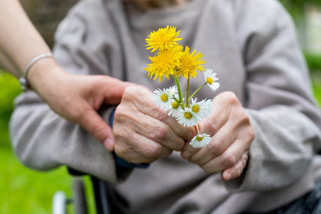 A caregiver holds onto her elderly mother as she shows off some wildflowers