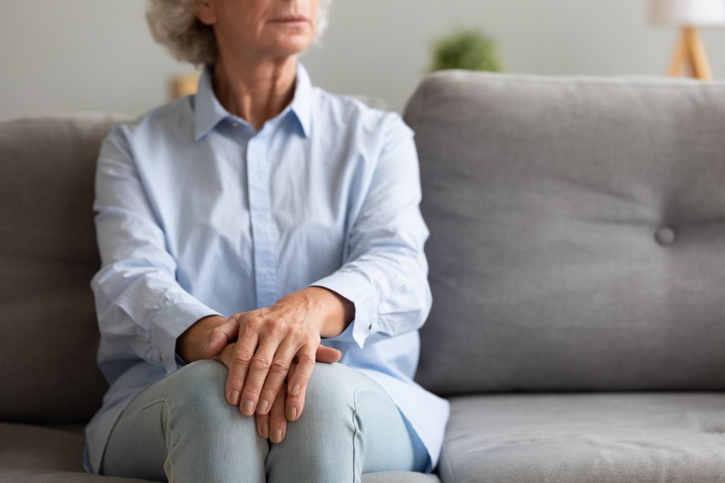 An elderly lady sitting on a couch with her hands together