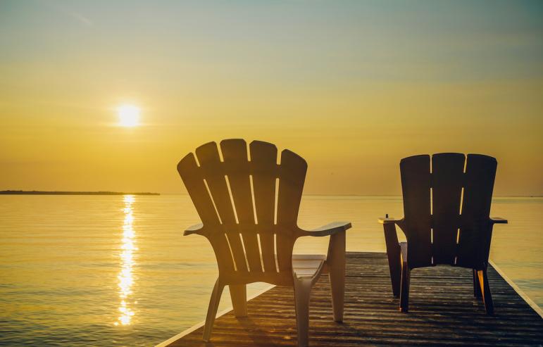 Two lawn chairs sitting on a dock overlooking the ocean at sunset