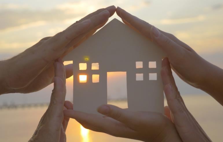 Caregiver hands in front of a sunset, holding the outline of a paper house