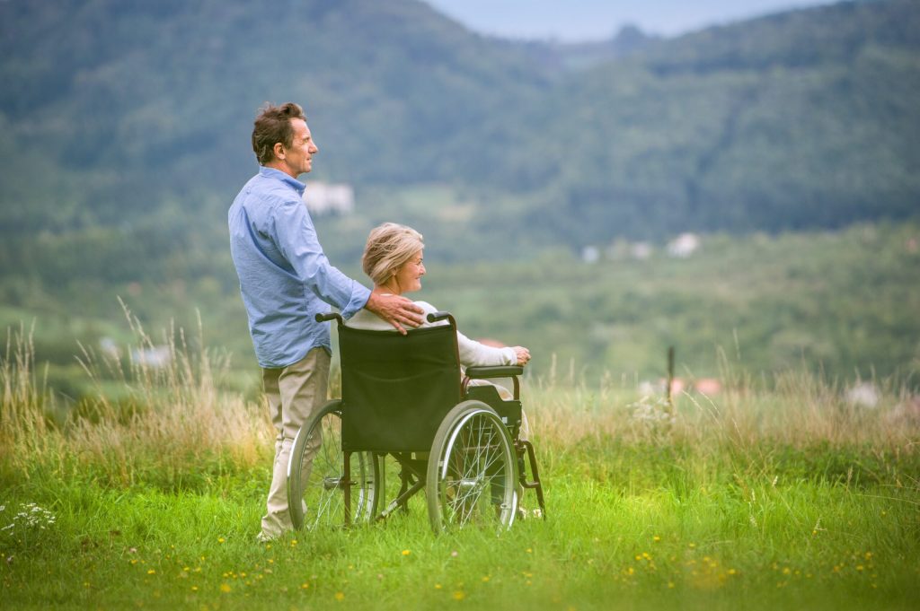 A caregiver husband and his wheelchair-bound wife looking off into the scenic mountains