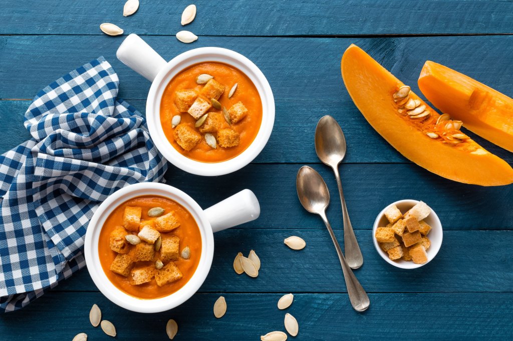 Two bowls of healthy squash soup with croutons and seeds on a wooden table