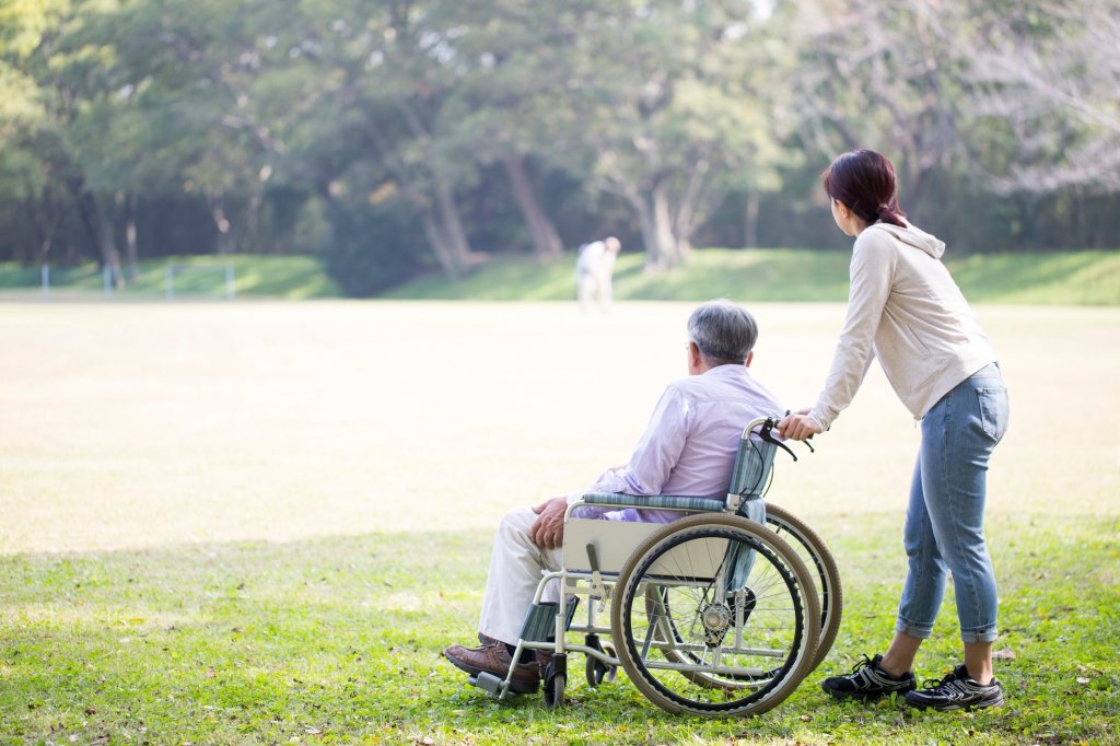 A caregiver pushes her wheelchair-bound father around the park