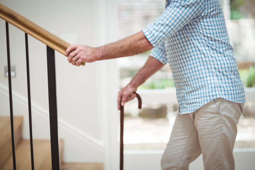 An elderly man with a cane trying to walk up the staircase alone