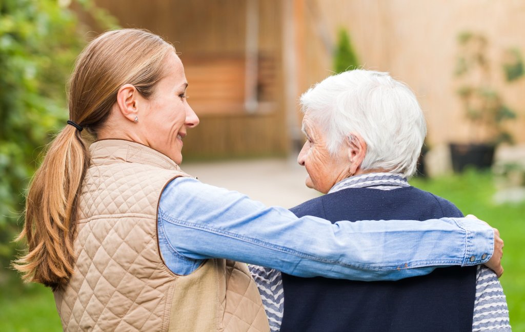 A caregiver daughter with her arm wrapped around her elderly mother's shoulders