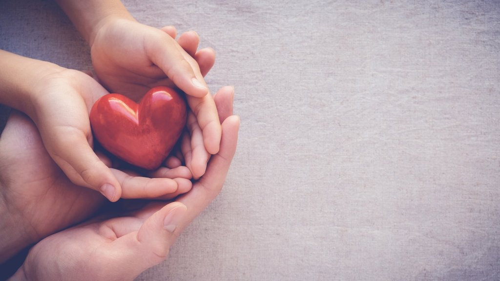 Adult's hands cradle a child's hands, holding a heart-shaped object