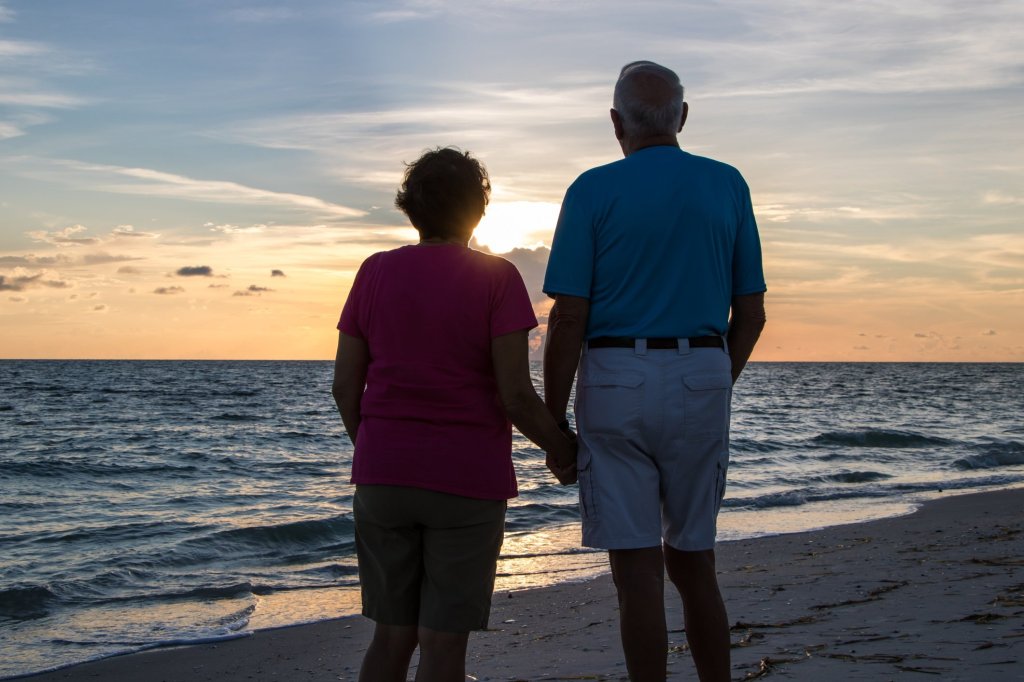 A retired couple holding hands on a beach, gazing into the sunset