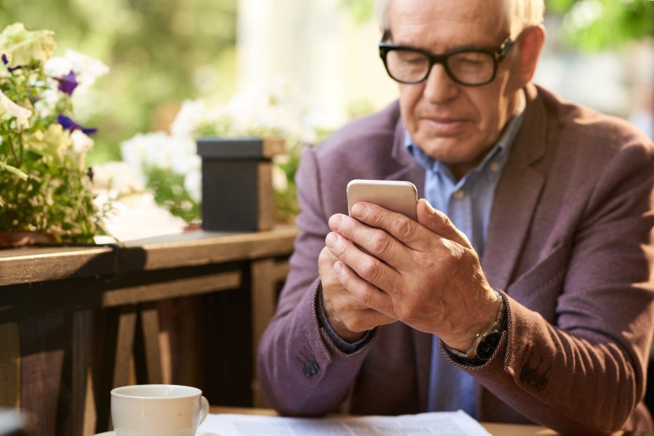 An elderly caregiver taking time for lunch while using his smartphone
