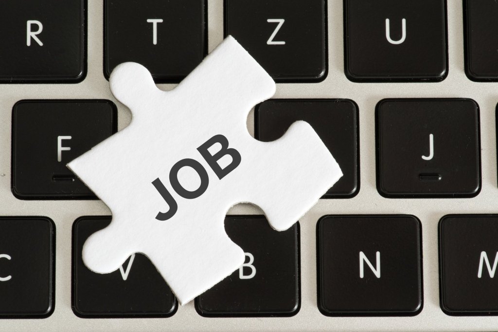 A puzzle piece with the word job written on it sitting on top of a computer keyboard