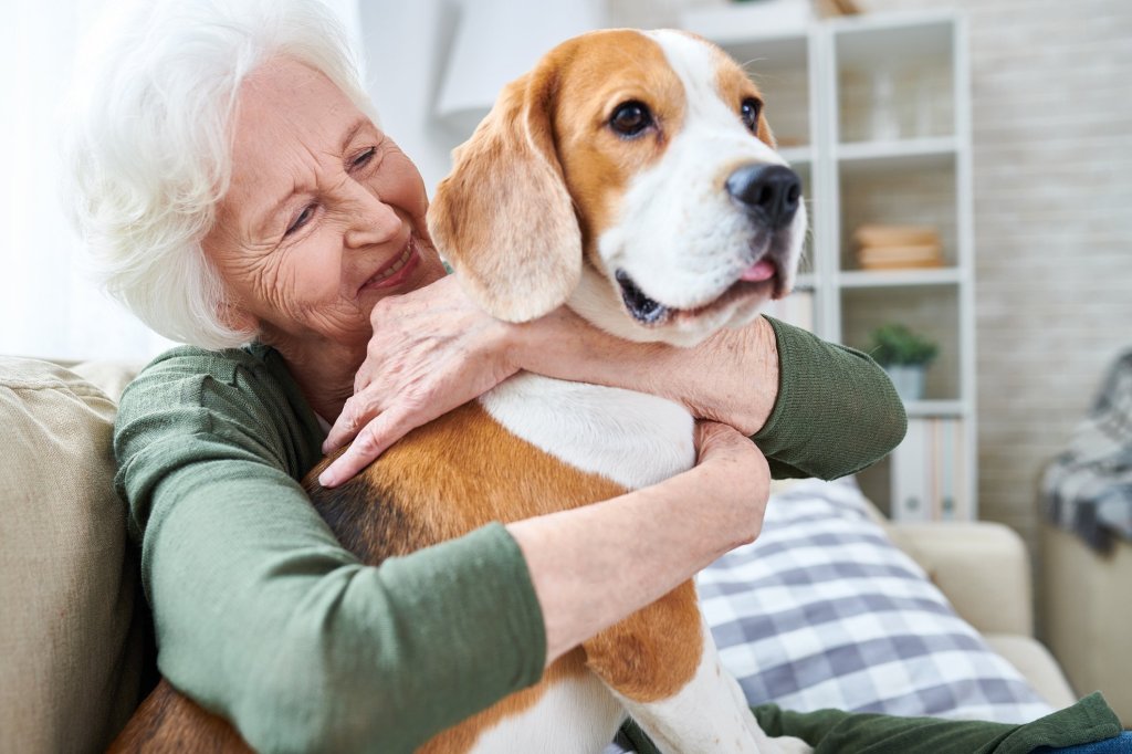 An elderly lady smiling as she hugs her dog representing the importance of companionship