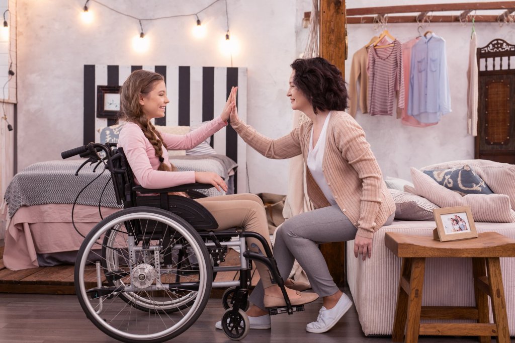 A caregiver mother high fiving her wheelchair-bound daughter