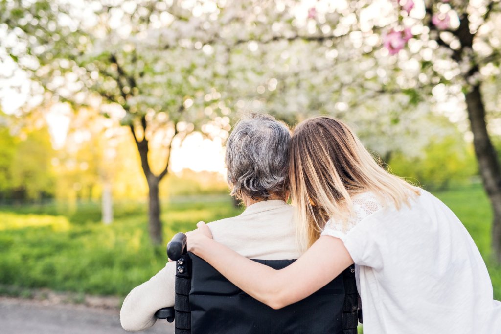 A caregiver with her arms wrapped around her elderly wheelchair-bound loved one