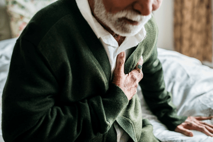An elderly man holding his chest, highlighting the importance of recognizing and addressing health needs in caregiving