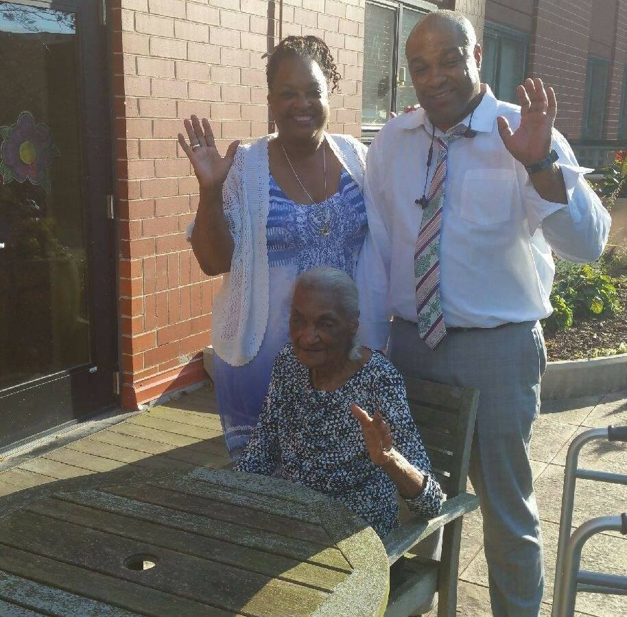 A caregiver daughter posing for a picture with her husband and elderly mother