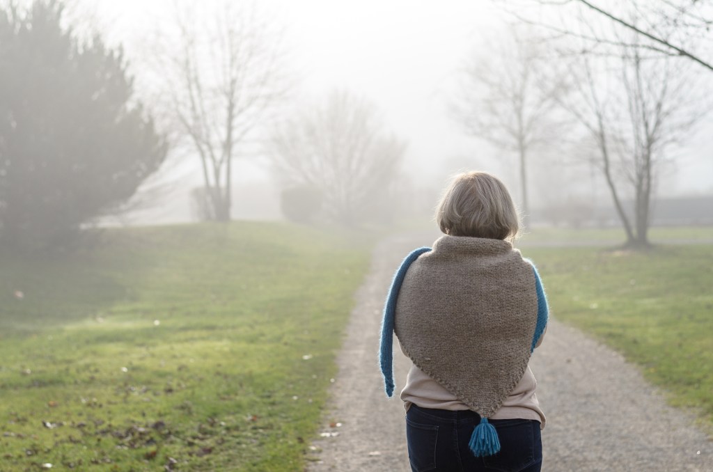 An elderly lady gazes into a foggy path, symbolizing the journey of caregiving with uncertainty and resilience