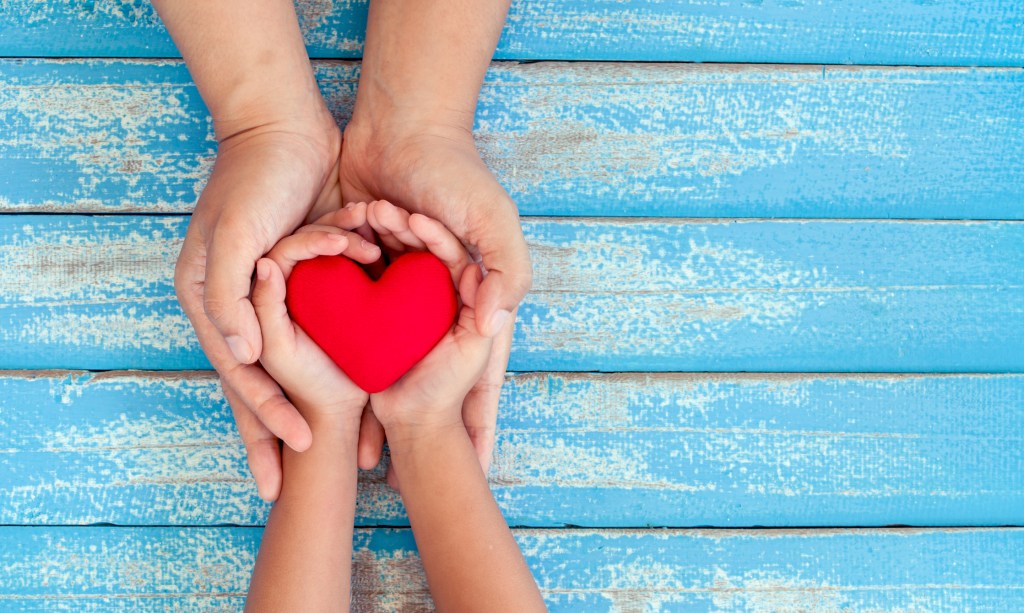 Gentle adult hands cradling a child's hands shaping a clay heart, symbolizing nurturing and guidance