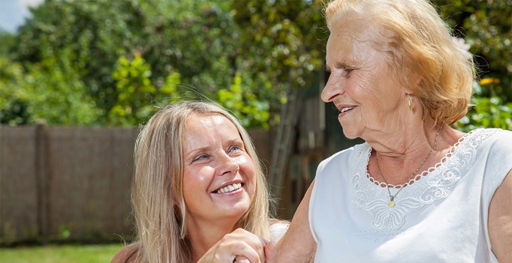 A caregiver and her mother smiling while sitting outside on beautiful day