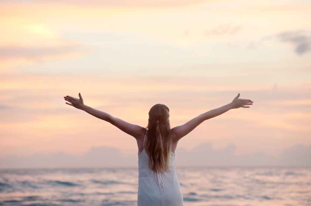 A person with arms outstretched in front of the ocean, giving the sense of accomplishment in caregiving advocacy.