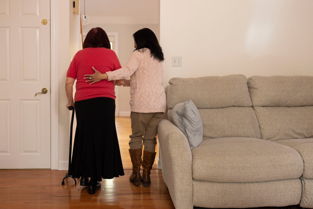 A caregiver helps her month walk.