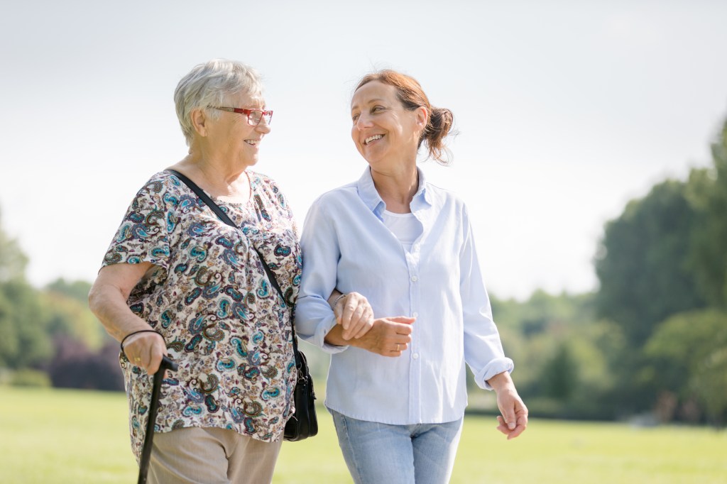 Happy senior woman and caregiver walking outdoors