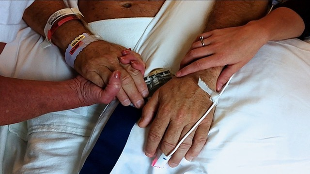 Close-up of family members holding hands with a loved one in a hospital bed, showing support and connection during recovery after a serious injury.